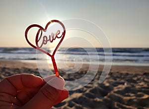 Person holding fingers hand stick shape red heart and word Love background sea