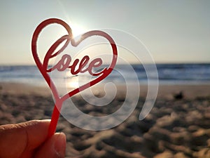 Person holding fingers hand stick shape red heart and word Love background sea