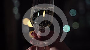 Person holding glass of champagne, lights blur background. Citylights or light string garland