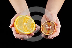 Orange and blood or red orange fruit halves in hands on black background