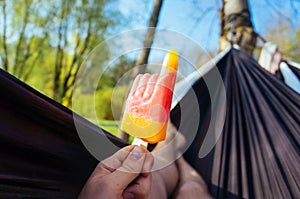 Person holding an ice fruit popsicle lying in a hammock