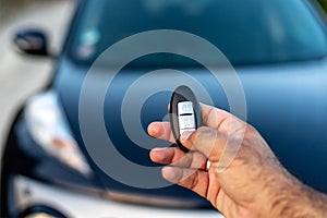 A person holding a keyless car remote in his hand by pressing the unlock button. selective focus with blurred background