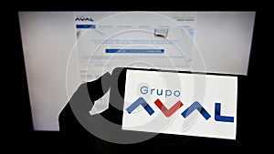 Person holding mobile phone with logo of Colombian Grupo Aval Acciones y Valores S.A. on screen in front of web page.