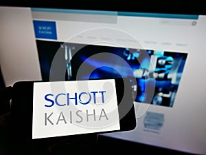 Person holding mobile phone with logo of Indian packaging company Schott Kaisha Pvt. Ltd. on screen in front of web page.
