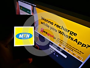 Person holding mobile phone with logo of South African telecommunications company MTN Group on screen in front of web page.