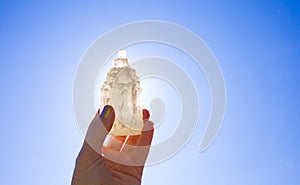 Person holding naturally carved mineral stone Selenite tower against sun and blue sky, stone has healing and cleansing properties. photo