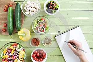 Person holding pencil and writing recipe in cookbook while cooking