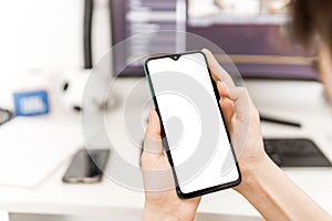 Person holding phone with blank screen in hands at work desk