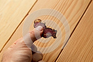 Person holding a piece of biltong with a wooden surface in the background