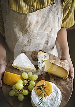 Person holding a platter of green grapes and different types of cheese