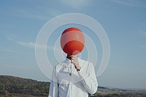 Person holding a red balloon in front of his face photo