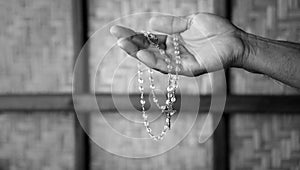 Person holding a rosary in hand in black and white background with light. Praying rosary concept.