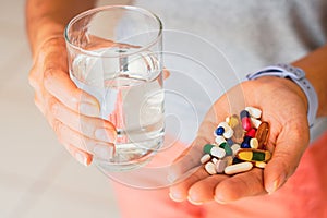 A person holding several medicine pills and a glass of water