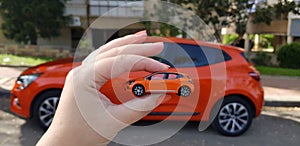 Person holding small car model against real car of same type