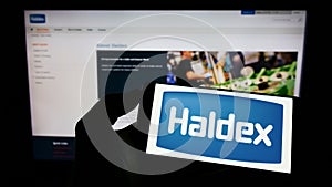 Person holding smartphone with logo of automotive company Haldex Europe SAS on screen in front of website.