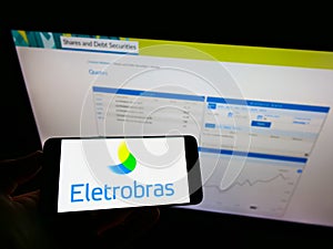 Person holding smartphone with logo of Centrais ElÃÂ©tricas Brasileiras S.A. (Eletrobras) on screen in front of website.