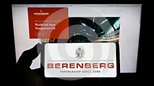 Person holding smartphone with logo of German bank Joh. Berenberg, Gossler Co. KG on screen in front of website.