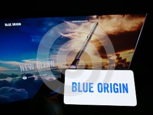 Person holding smartphone with logo of US aerospace company Blue Origin LLC on screen in front of website.