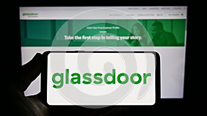 Person holding smartphone with logo of US job review company Glassdoor Inc. on screen in front of website.