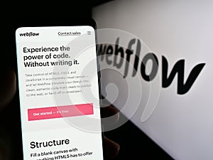 Person holding smartphone with web page of US web development software company Webflow Inc. on screen with logo.
