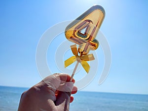 Person holding stick shiny golden number 4 four hand backdrop waves blue sea sky photo