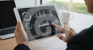 A person is holding a tablet displaying various data visualizations, including bar