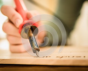 Person Holding a Wood Burning Tool, Burning Letters onto Wood