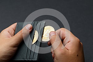 A person holds Bitcoin coins. A businessman puts bitcoin gold coins into a wallet. Bitcoin purchase concept. Bitcoin and wallet