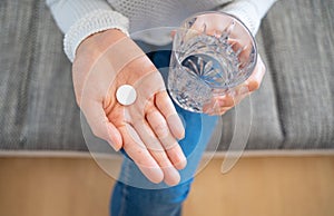 Person holds a glass of water with a round white tablet in hand