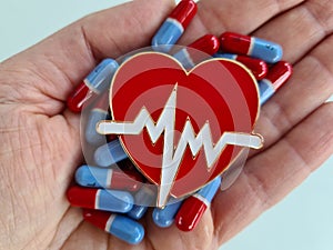 Person holds heart pills and cardiological heart in hand photo