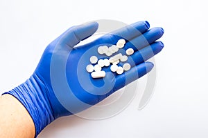 Person holds in his hand in palm dressed in medical latex glove, white pills and tablets. Concept photo for use in medicine, pharm