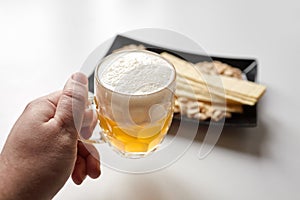 Person holds a mug of unfiltered light wheat beer, beer snacks on white table