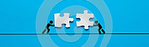 Person icons are pushing and joining the puzzle pieces. Sustaining cooperation, teamwork, unity, togetherness, synergy or