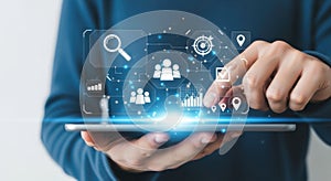 Person interacting with futuristic digital interface featuring business and data icons on a tablet