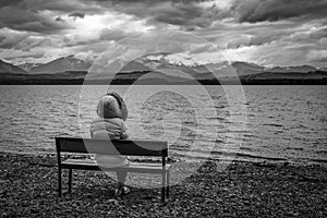 Person in jacket sitting on bench on the shore of the lake