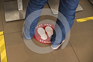 A person in jeans and slippers stands casually on a social distancing sticker at a fast food restaurant.