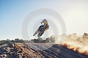 Person, jump and sports motorcyclist in the air for trick, stunt or race on outdoor dirt track. Rear view of expert