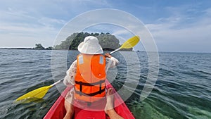 A person in a kayak paddling towards a small island in the distance under a clear blue sky on a calm day