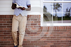 Person leaning against a wall while reading the bible