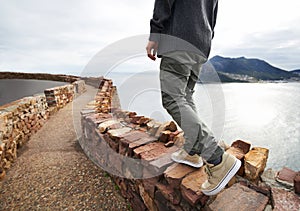 Person, legs and mountain cliff at ocean for explore nature for vacation journey or adventure, walking or relax. Shoes