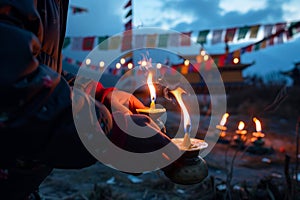 person lighting butter lamps with prayer flags in background in dusk
