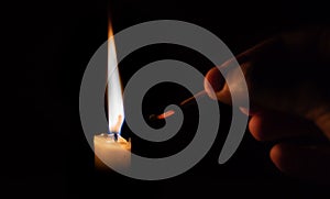 Person lighting a candle with a matchstick about to extinguish the matchstick