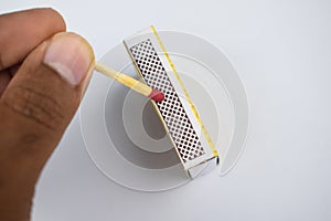 A person lighting a single match sticks by swiping the match with the box