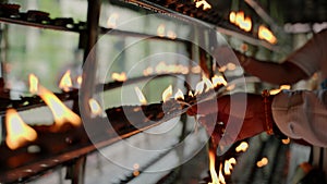 Person lights oil lamps for religious ritual in Buddhist temple. Devotees perform traditional offerings in sacred