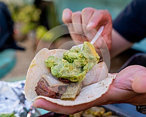 person making a delicious Mexican style carne asada taco with avocado and salsa