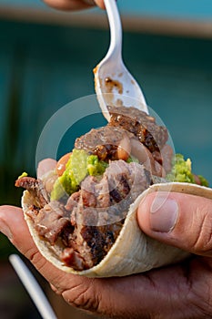 person making a delicious Mexican style carne asada taco with avocado and salsa