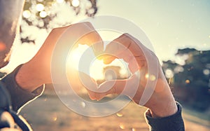 Person making heart with hands over nature sunset background. Happy young people. Silhouette hand in heart shape with sun inside photo