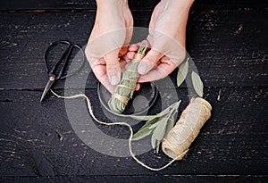 Person making white sage Salvia apiana smudge stick at home with homegrown sage leaves.