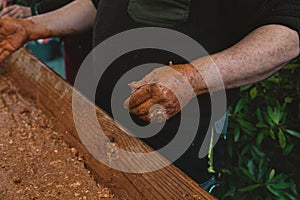 Person mashing meat with hands in a wooden pot under the lights with a blurry background