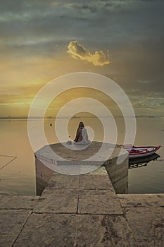 A person is watching beautiful sunrise on the bank of river ganga at ghats of varanasi while meditating